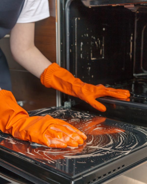 Kitchen cleaning. Girl's hands in gloves wash clean the stove, kitchen oven in the kitchen