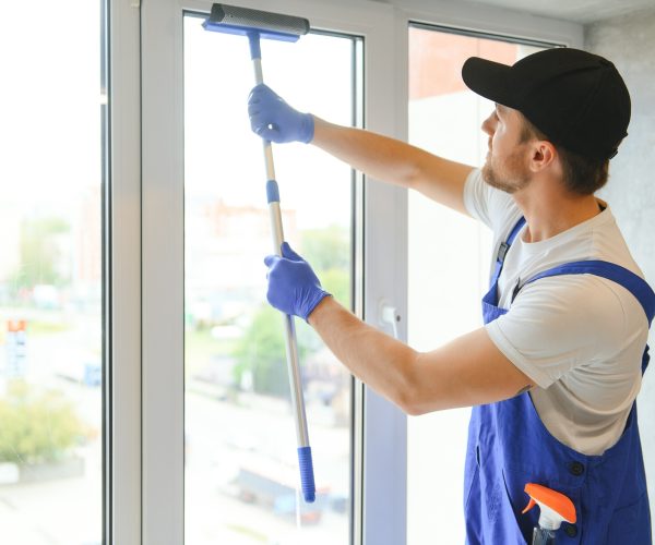 Male professional cleaning service worker in overalls cleans the windows.